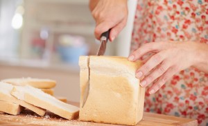 Close Up Of Woman Slicing Loaf Of Bread In Kitchen