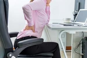 woman rubbing back at work desk, 7 ways to get rid of back pain, by healthista