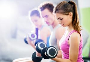 Three people lifting dumbbells in a gym. Focus is on foreground. 