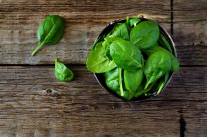 spinach in the bowl on the dark wood background. toning. selective focus on the lower right leaf