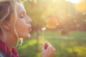 Close-up of a happy young blonde woman blowing dandelion