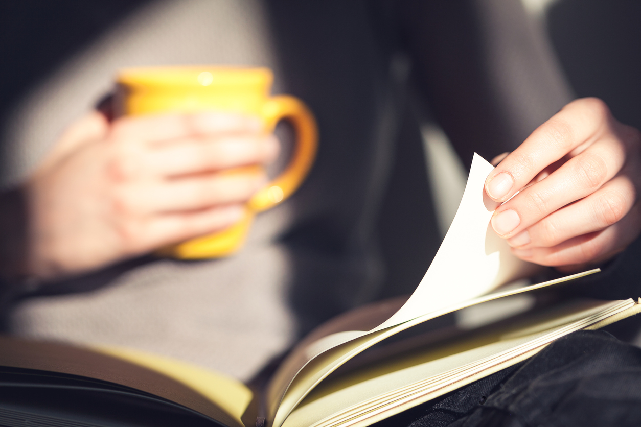 woman-holding-yellow-mug-turning-page-book-novels-that-changed-your-life-healthista-body-image5.jpg