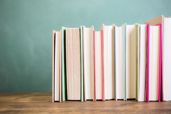 School books stacked on desk with chalkboard.